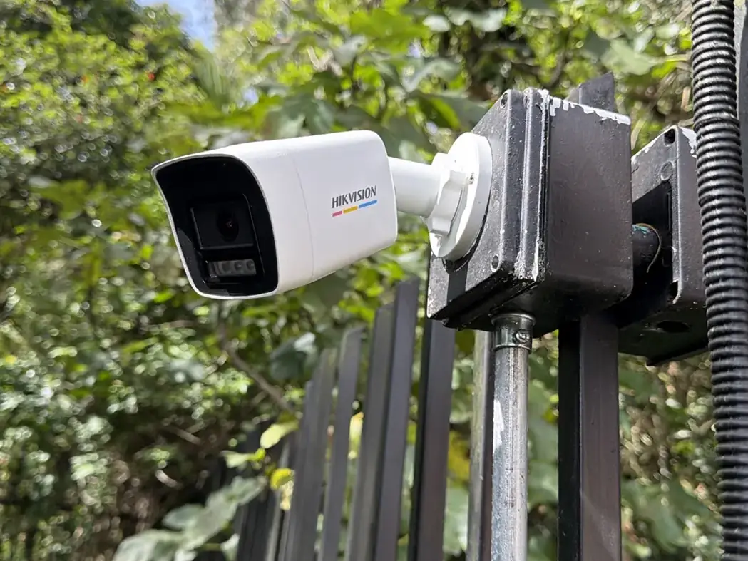 Cámara bullet Hikvision sobre la reja, con el jardín al fondo