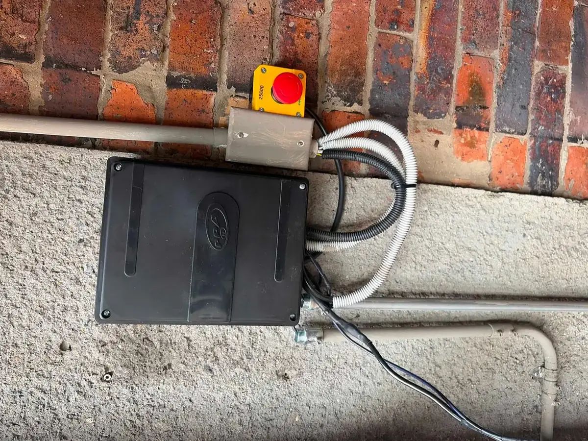 Caja de control de la puerta vehicular con pulsador de parada, sobre muro de ladrillo