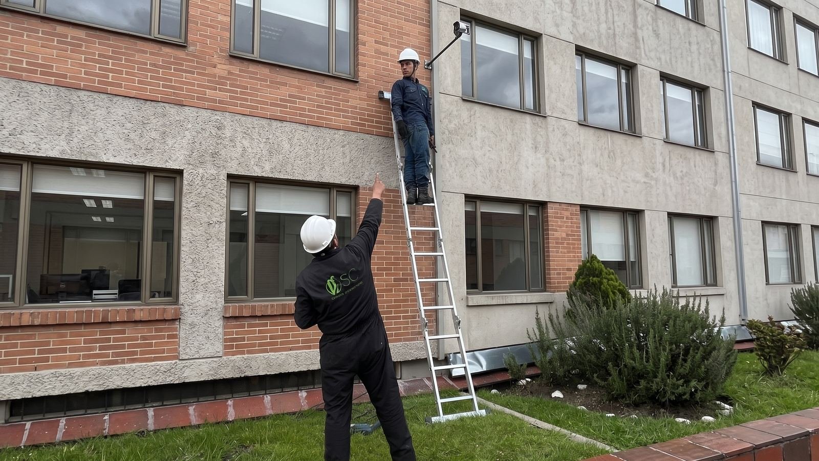 Técnico de SC instalando una cámara en fachada, con un compañero asegurando la escalera